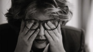 A woman wiping her eyes under her glasses.