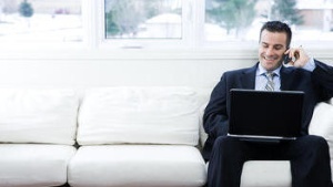 Man sitting on a couch with a laptop and talking on phone.