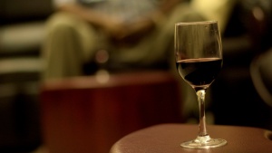 A glass of wine in the foreground and person sitting the background