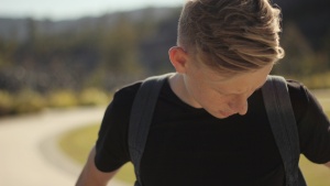 A young man looking down wearing a backpack.