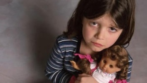 A small girl with a scared face holding a doll.