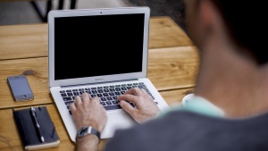 A man typing on a laptop while sitting a desk.