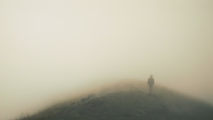 A man on top of hill that is surrounded in fog.