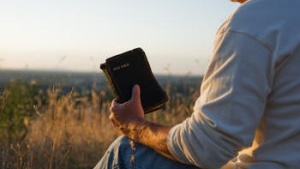 A man sitting on the ground holding an old Bible.