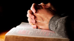 Hands clasped onto of a Bible as if person is praying.