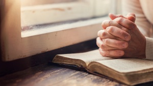 A woman reading a Bible by a window.