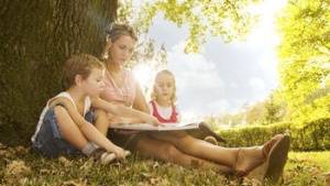 A mother reading to two children sitting outside.