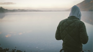 A young man standing by a lake.