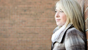 A teenage girl standing by a brickwall.