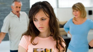 Teen girl in foreground with upset parents in background
