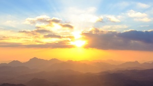 Sunset over a mountain range with clouds in the foreground.