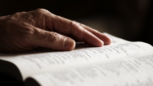 An older man's hand on an open Bible.