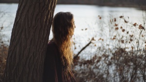 A young woman leaning up against a tree.