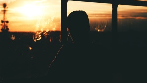 A young man looking out a window with the sun setting.