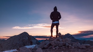 A person standing on top of a rocky hill watching the sunset.
