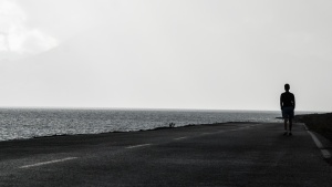 A man walking on a road beside a body of water.