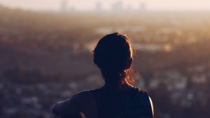 A woman sitting by herself on a cliff looking out over the town. 