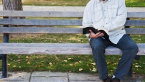 A man sitting on a bench reaching the Bible.