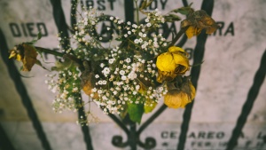 A tombstone with an iron fence and dried flowers in front of it.