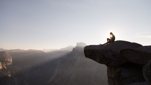 A person sitting on a cliff with sunset behind.