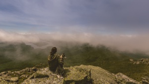 A woman sitting on cliff edge with her dog.