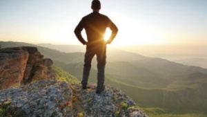 A young man standing at the edge of cliff looking at the setting sun.