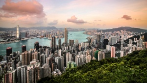 a city with green trees on the outskirts, skyscrapers and buildings, and a body of water running through the center.