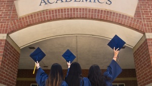 three girls in graduation robes holding up their caps underneath the archway of an academic institution
