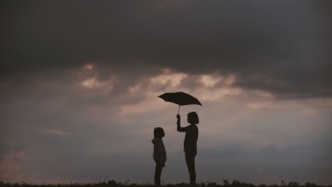 Photo of a girl holding an umbrella over another girl.