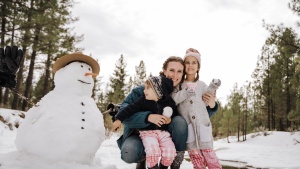 a woman hugging a boy and a girl as they stand beside a snowman