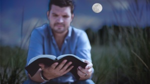 A man reading a Bible in the light of a full moon