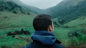 a man looks towards a mountain landscape that slopes up both to the right and to the left