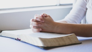 a pair of folded hands on an open Bible