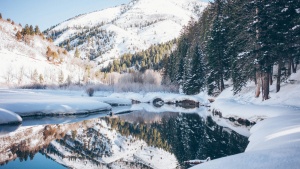 a winter mountain landscape with snow that is reflected in a body of water below