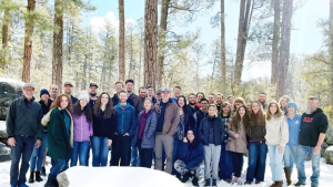 A group of young adults gathered outdoors in the snow with trees in the background