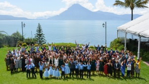 a group of people standing outdoors on the grass with mountains outlined in the background beyond a body of water