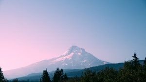 a dark landscape in the foreground, behind which stands a mountain with a pink-blue sky in the background