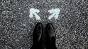 Photo of a person's feet standing in front of two arrow pointing in different directions, connoting a choice.