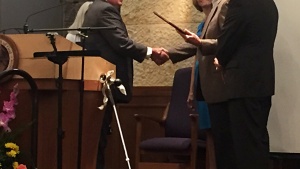 Randy Schreiber receiving the engraved plaque and shaking hands with Mike Miller. 