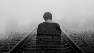 Photo of depressed man on railroad tracks.