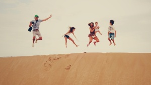 A family jumping up from a sand dune.