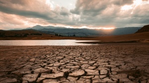 a landscape at sunset featuring an expanse of parched ground in the foreground, contrasted with a small body of water and rolling hills in the background