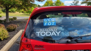 the rear window of a red car with a sticker that reads "UCG FOT" prominently displayed over the "Beyond Today" sticker