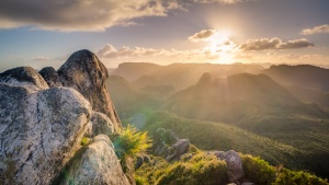 Photo of the sun shining over a mountain.