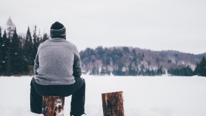 A man sitting on a log starring at the snow.