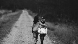 Black and white photo of two children walking down a road, each with an arm around the other's shoulders.