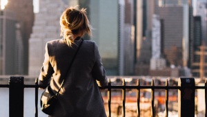 A woman leaning against an iron fence looking over the skyline of a city.