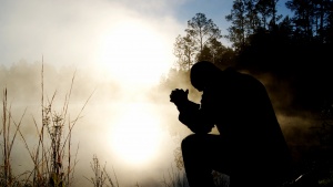 A man praying outside by a field lit by the morning sun.