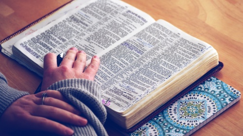 A woman with an open Bible laying on a table.