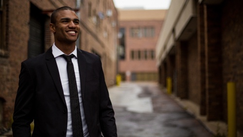 a man wearing a suit and tie standing with a road and buildings in the background